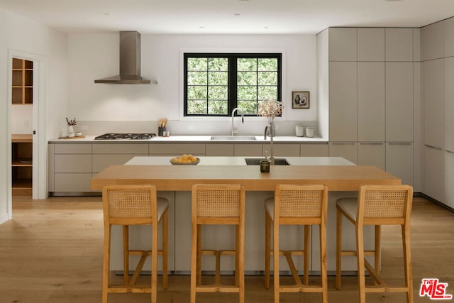 kitchen featuring a breakfast bar, sink, wall chimney exhaust hood, light wood-type flooring, and stainless steel gas cooktop