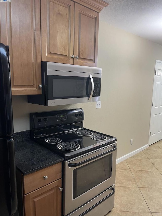 kitchen featuring appliances with stainless steel finishes, dark stone counters, and light tile patterned flooring