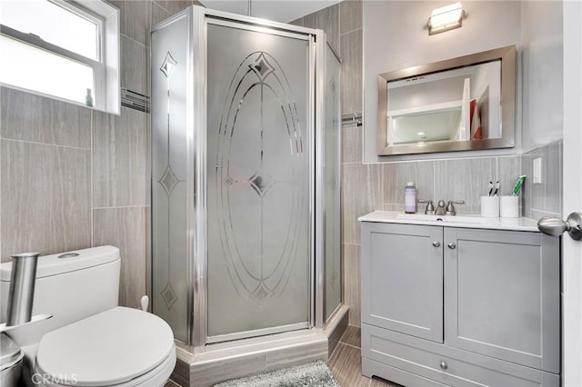 bathroom featuring vanity, a shower with door, tile walls, and toilet