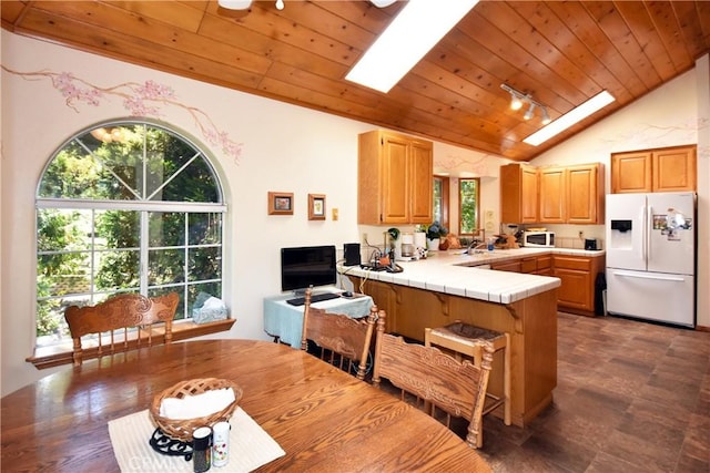 kitchen with vaulted ceiling with skylight, wood ceiling, tile countertops, a peninsula, and white appliances