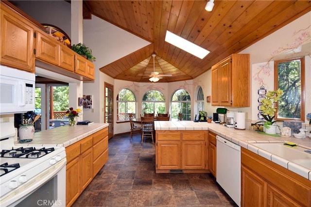 kitchen with white appliances, vaulted ceiling with skylight, wooden ceiling, kitchen peninsula, and tile counters