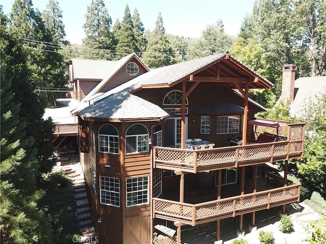 back of property featuring stairway, a deck, and a shingled roof
