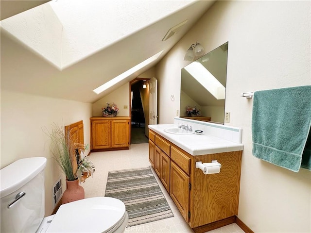 bathroom with vaulted ceiling with skylight, vanity, and toilet