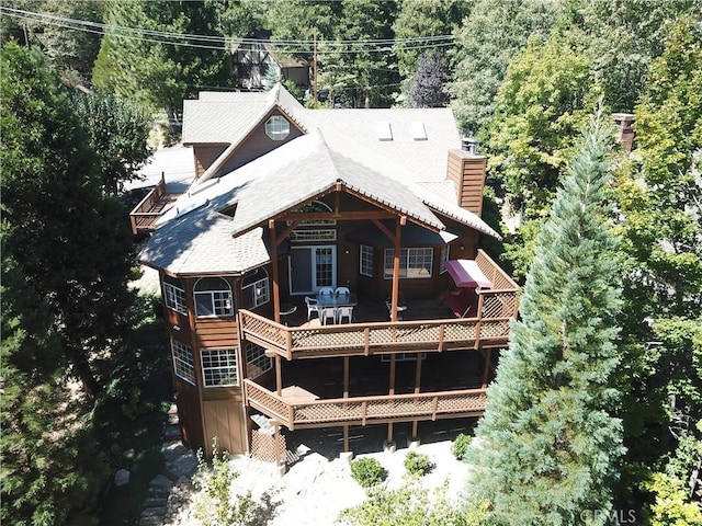 back of property featuring a wooden deck, a chimney, and a forest view