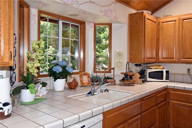 kitchen featuring brown cabinetry, white microwave, light countertops, a sink, and vaulted ceiling