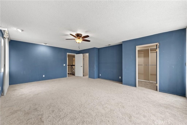 unfurnished bedroom featuring carpet flooring, ceiling fan, a spacious closet, a textured ceiling, and a closet