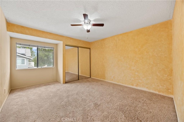 unfurnished bedroom featuring carpet flooring, a textured ceiling, a closet, and ceiling fan