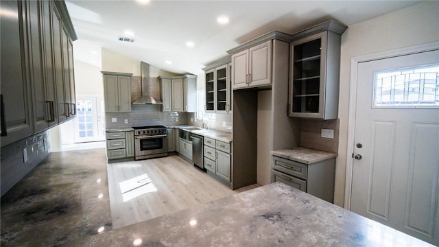 kitchen featuring gray cabinetry, wall chimney exhaust hood, tasteful backsplash, vaulted ceiling, and appliances with stainless steel finishes