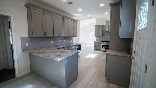 kitchen with decorative backsplash, appliances with stainless steel finishes, wall chimney exhaust hood, light hardwood / wood-style flooring, and lofted ceiling