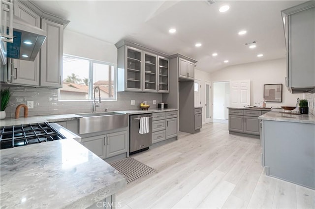 kitchen featuring light wood finished floors, glass insert cabinets, gray cabinetry, stainless steel dishwasher, and a sink