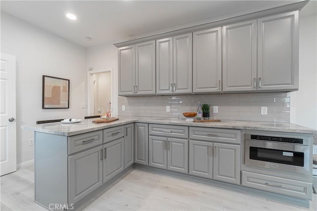 kitchen featuring light wood finished floors, gray cabinets, backsplash, oven, and a peninsula