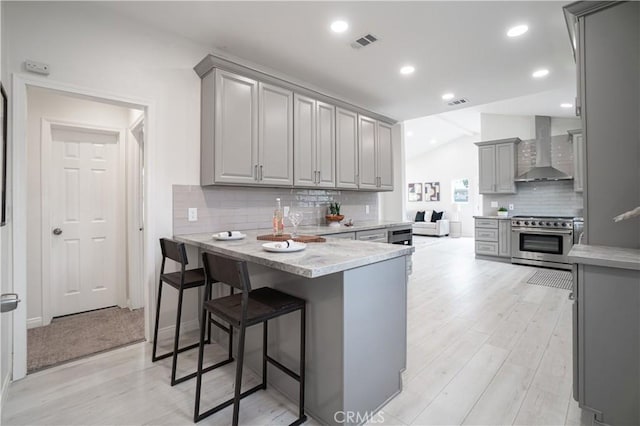 kitchen with gray cabinetry, a peninsula, visible vents, wall chimney range hood, and high end stainless steel range oven