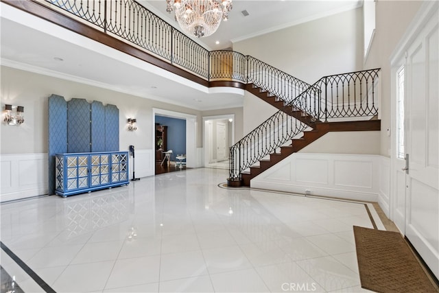 foyer with ornamental molding, a high ceiling, a notable chandelier, and light tile patterned floors