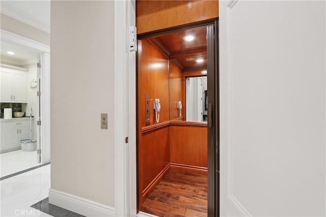 corridor with light hardwood / wood-style floors, crown molding, elevator, and wood walls