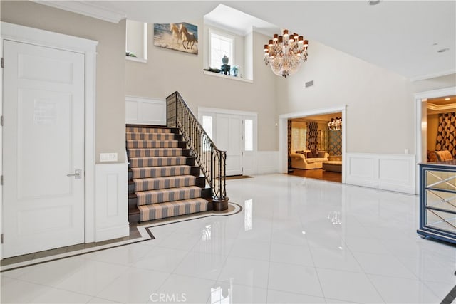 entryway with crown molding, a notable chandelier, light tile patterned floors, and a high ceiling