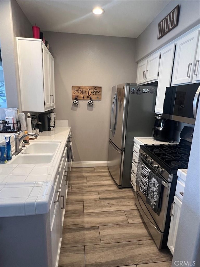 kitchen with appliances with stainless steel finishes, light hardwood / wood-style flooring, white cabinetry, and sink