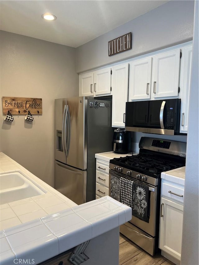 kitchen with tile countertops, sink, light wood-type flooring, appliances with stainless steel finishes, and white cabinetry