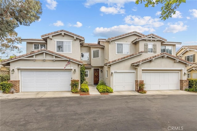 view of front of home featuring stucco siding, driveway, a tile roof, and a garage