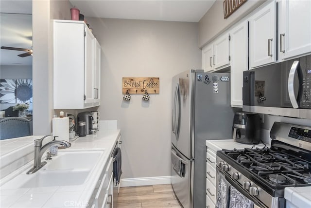 kitchen with ceiling fan, appliances with stainless steel finishes, a sink, tile counters, and white cabinetry