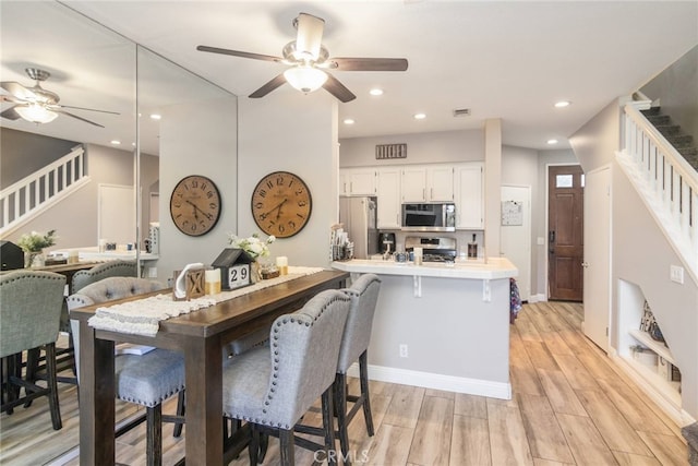 dining room with a ceiling fan, stairway, and light wood-style floors
