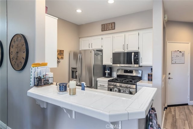 23014 Cheyenne Dr Unit 151, Valencia, CA 91354 - kitchen featuring stainless steel appliances, tile countertops, a peninsula, white cabinets, and light wood-style floors