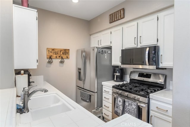 kitchen with tile counters, a sink, white cabinetry, and appliances with stainless steel finishes