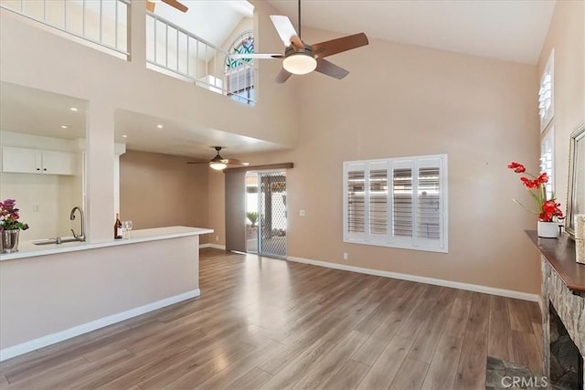 unfurnished living room with ceiling fan, sink, high vaulted ceiling, and light hardwood / wood-style floors