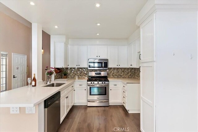 kitchen with kitchen peninsula, stainless steel appliances, sink, white cabinets, and dark hardwood / wood-style floors