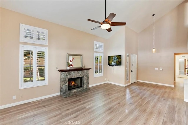 unfurnished living room with ceiling fan, a stone fireplace, high vaulted ceiling, and light hardwood / wood-style flooring