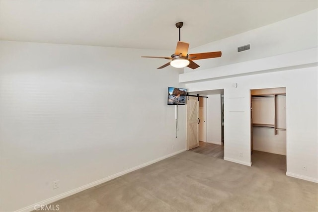 unfurnished bedroom with a barn door, light carpet, a closet, and ceiling fan