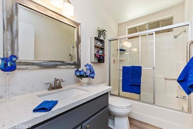 full bathroom featuring combined bath / shower with glass door, hardwood / wood-style floors, vanity, and toilet