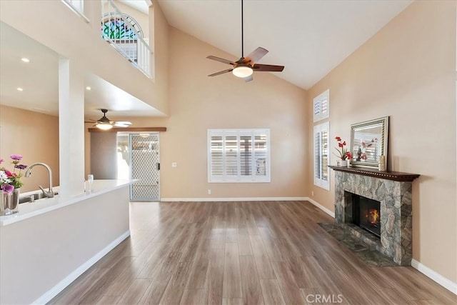 unfurnished living room with ceiling fan, sink, high vaulted ceiling, a fireplace, and hardwood / wood-style floors