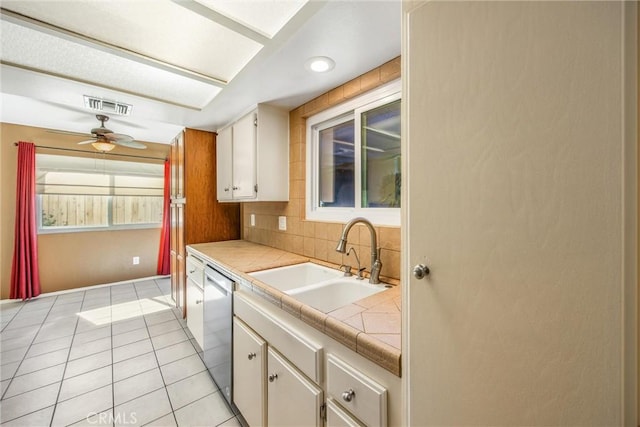 kitchen featuring sink, stainless steel dishwasher, ceiling fan, tile counters, and white cabinetry