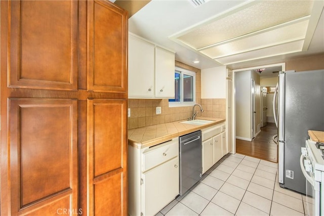 kitchen with stainless steel appliances, sink, light tile patterned floors, white cabinetry, and tile counters