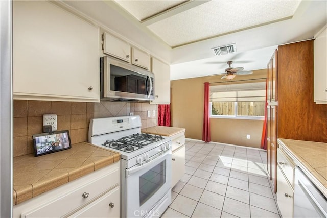 kitchen featuring tile countertops, ceiling fan, light tile patterned floors, tasteful backsplash, and white range with gas cooktop