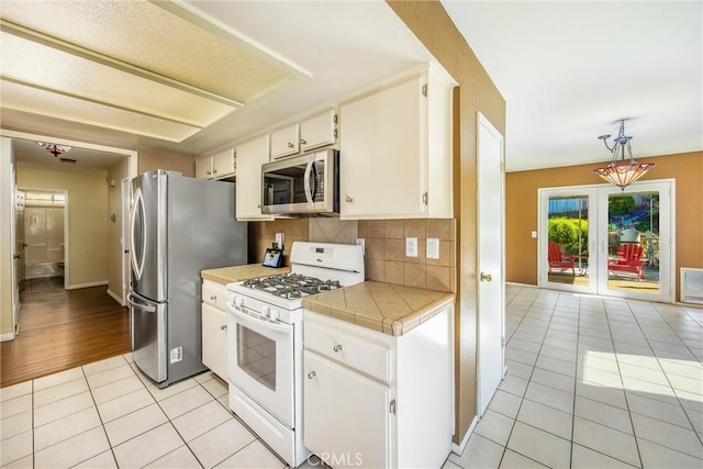 kitchen with decorative backsplash, appliances with stainless steel finishes, light tile patterned floors, and pendant lighting