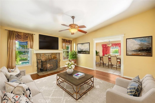 living room featuring hardwood / wood-style floors, ceiling fan, a stone fireplace, and lofted ceiling