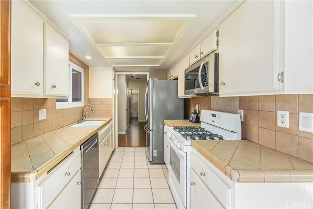 kitchen with tile countertops, white cabinetry, sink, and appliances with stainless steel finishes