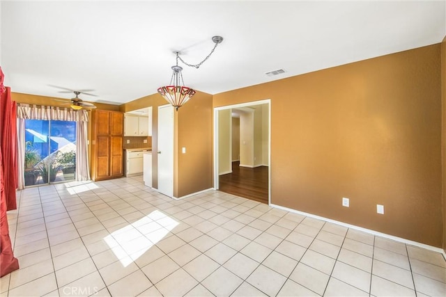 empty room featuring ceiling fan with notable chandelier and light tile patterned flooring