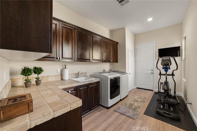 laundry room with cabinets, sink, light hardwood / wood-style floors, and washing machine and clothes dryer