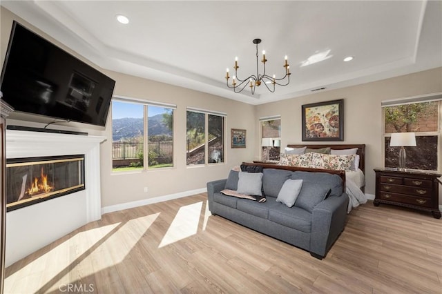 bedroom featuring an inviting chandelier, light hardwood / wood-style flooring, and a tray ceiling