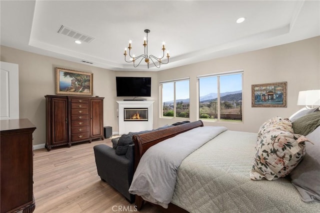 bedroom featuring a raised ceiling, light hardwood / wood-style flooring, and a notable chandelier