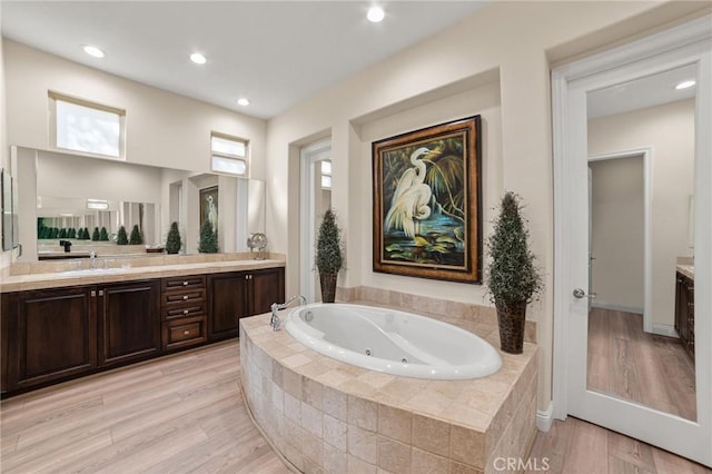 bathroom featuring vanity, a relaxing tiled tub, and hardwood / wood-style flooring