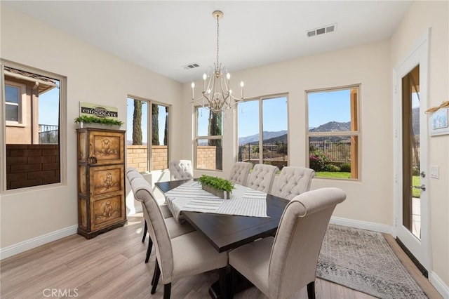 dining room with a mountain view, light wood-type flooring, a wealth of natural light, and a notable chandelier