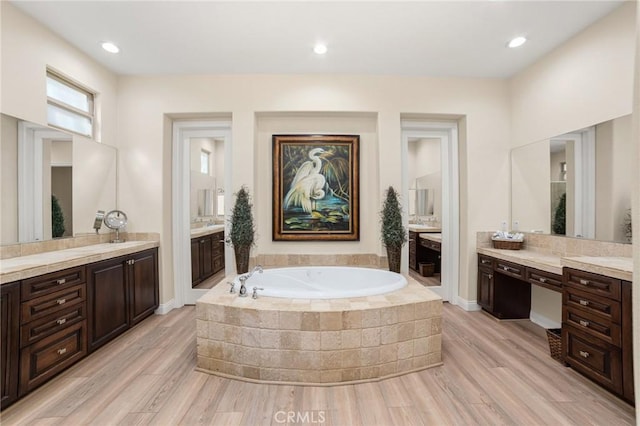 bathroom with wood-type flooring, vanity, and tiled bath