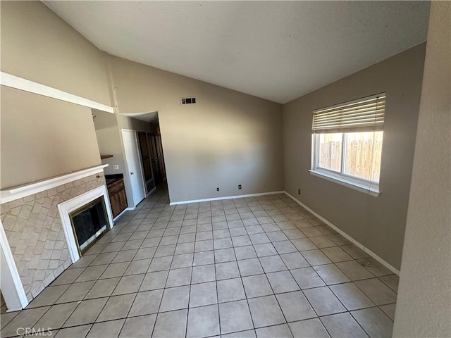 unfurnished living room with lofted ceiling, visible vents, a glass covered fireplace, and light tile patterned floors