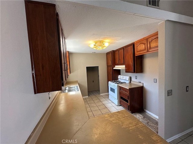 kitchen with white gas stove, light countertops, visible vents, and under cabinet range hood