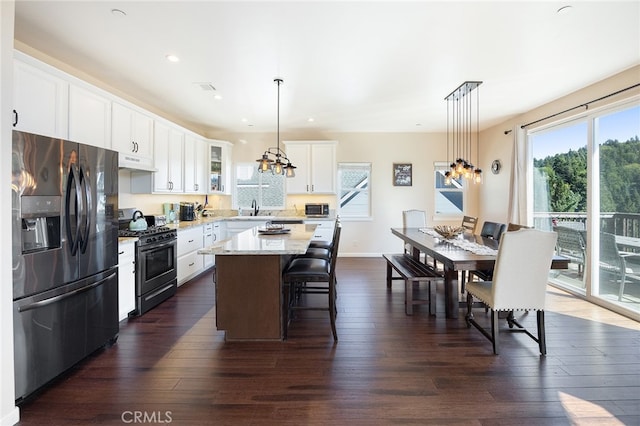 kitchen featuring black range with gas cooktop, stainless steel fridge, white cabinets, and pendant lighting