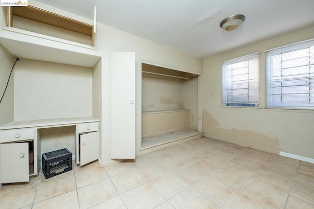 unfurnished bedroom with a closet, built in desk, and light tile patterned floors