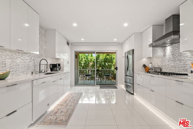 kitchen featuring wall chimney range hood, stainless steel appliances, sink, white cabinets, and tasteful backsplash